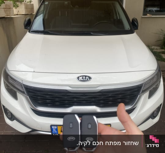מפתחות רכב קיה מוחזקים מול רכב לבן